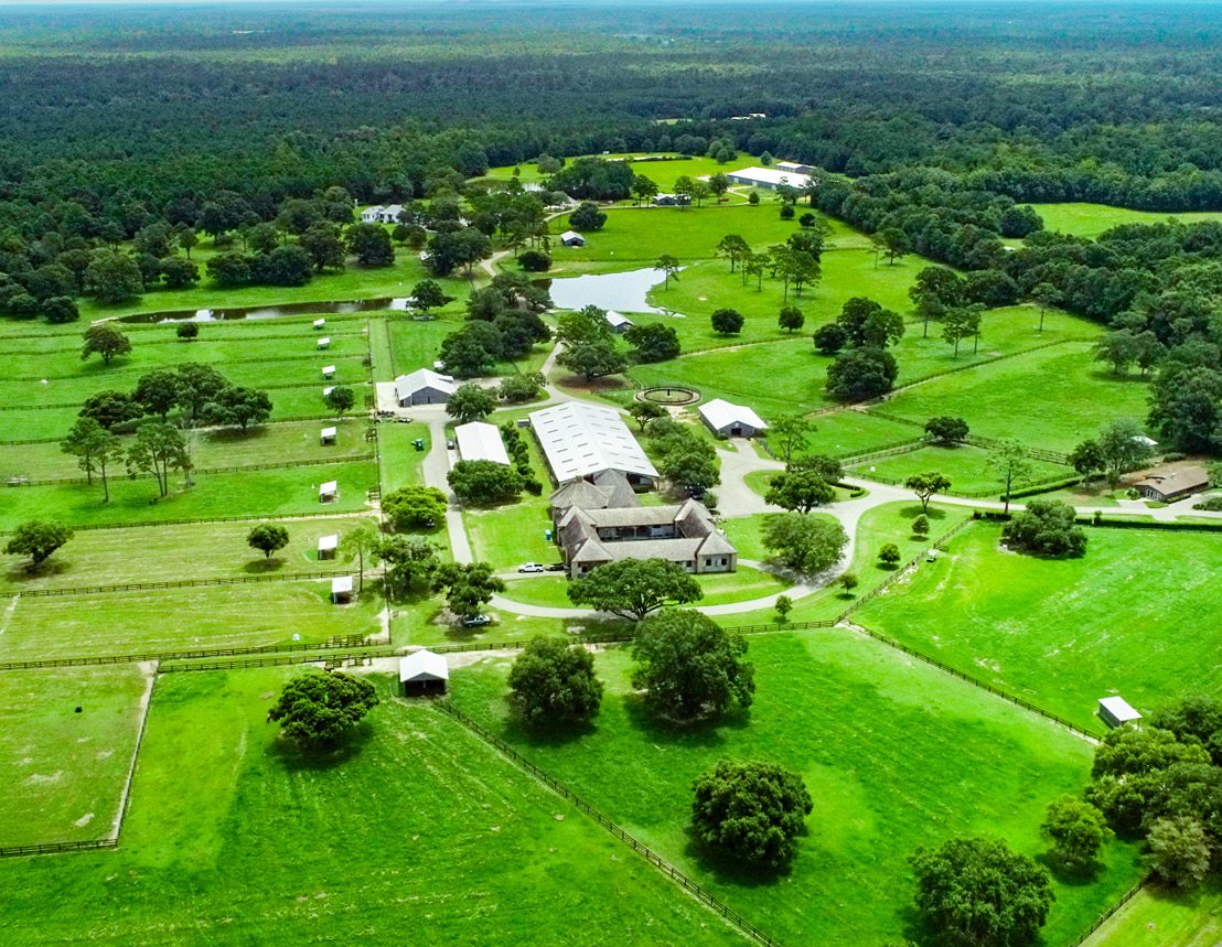 Twin Hills Ranch from the air — pastures, barns and arenas held inside a ring of hardwood timber