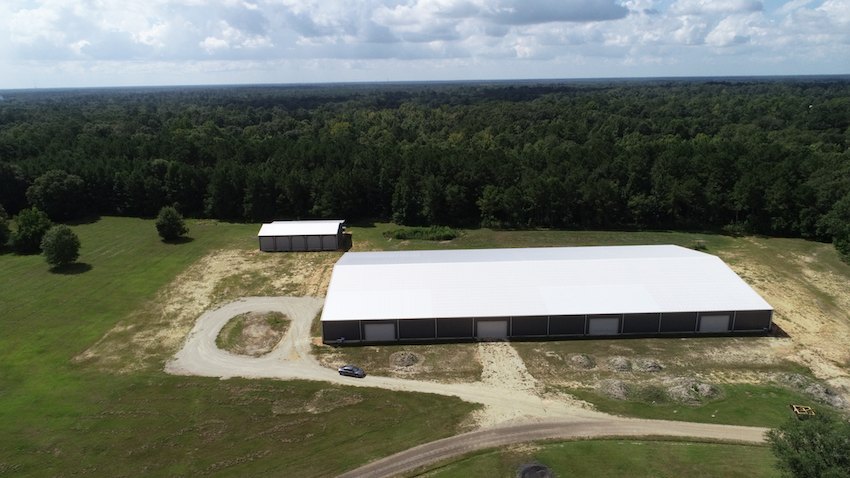 The covered arena complex seen from the air, set in open pasture against the tree line