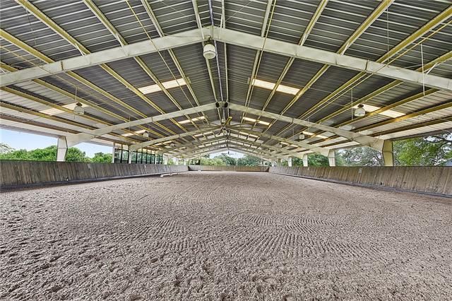 Open-air covered riding arena with steel trusses and a groomed sand floor