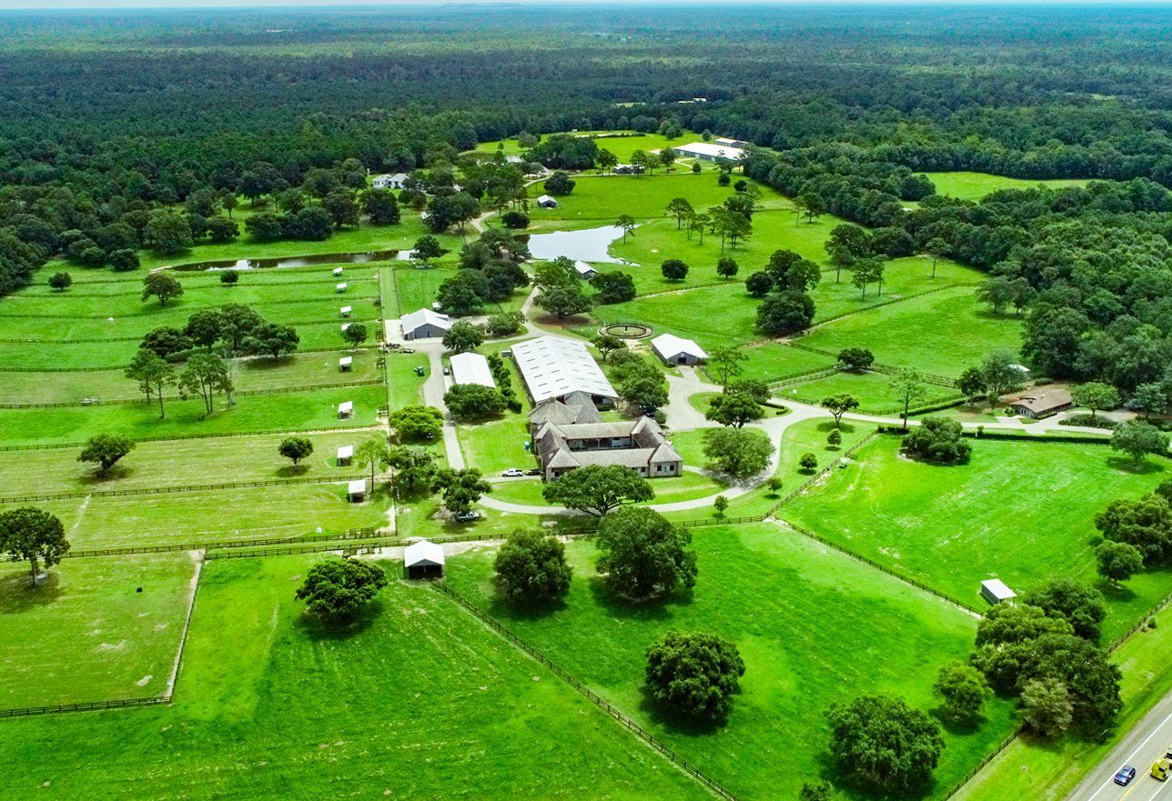 Aerial view of Twin Hills Ranch — the main residence, stables and arenas set among fenced pastures and hardwood timber